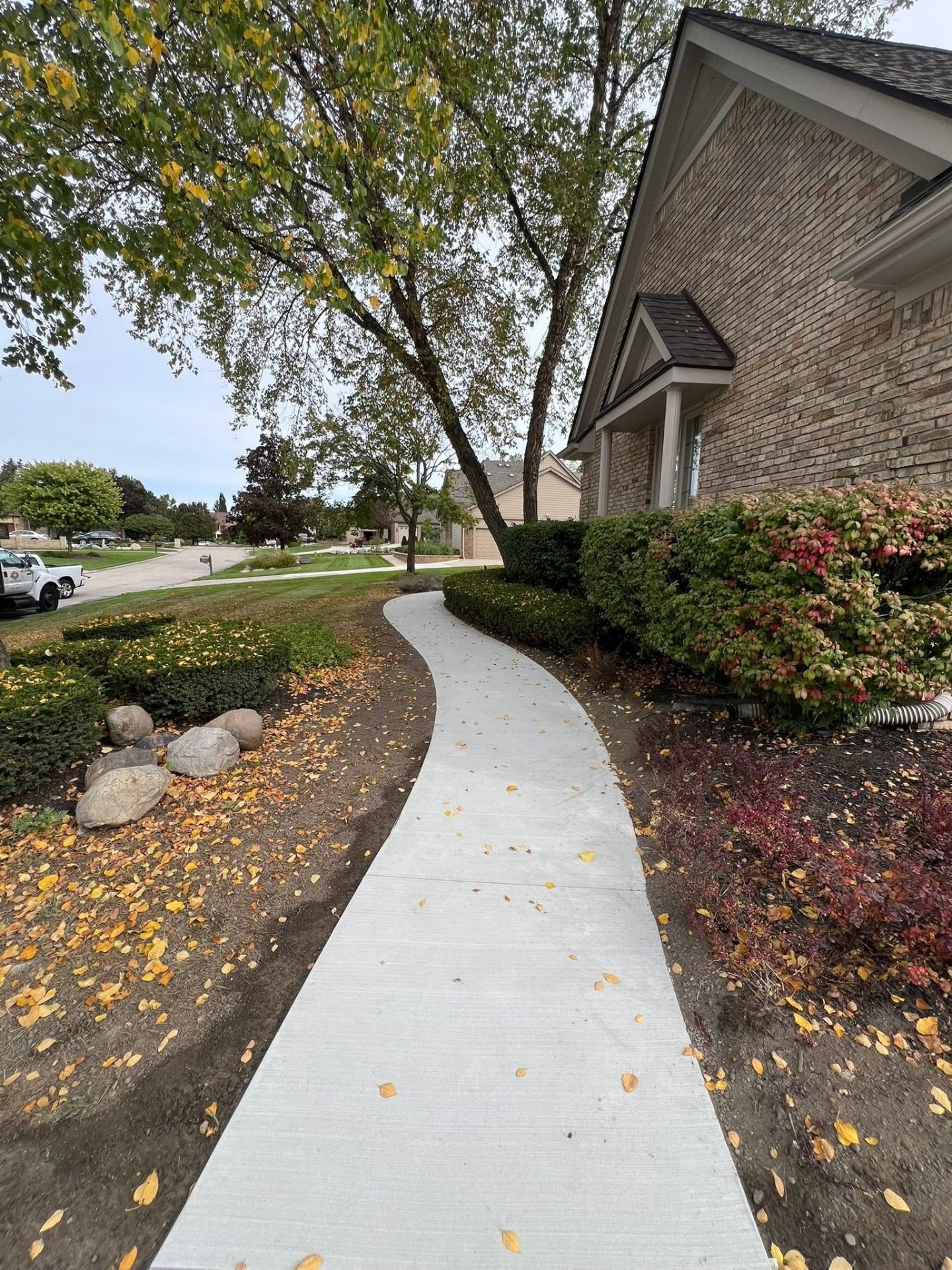 Curved concrete walkway with fall landscaping alongside a brick home